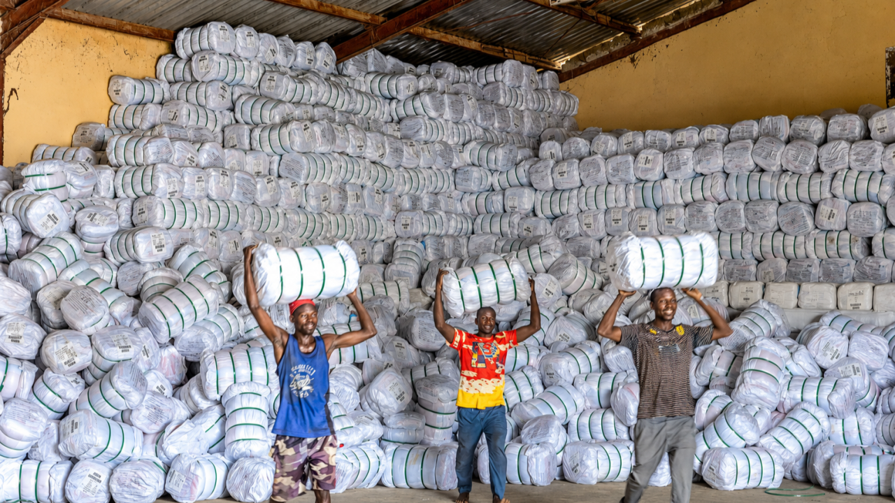 Warehouse workers lifting bales of insecticide-treated mosquito nets stacked floor to ceiling, ready for state distribution